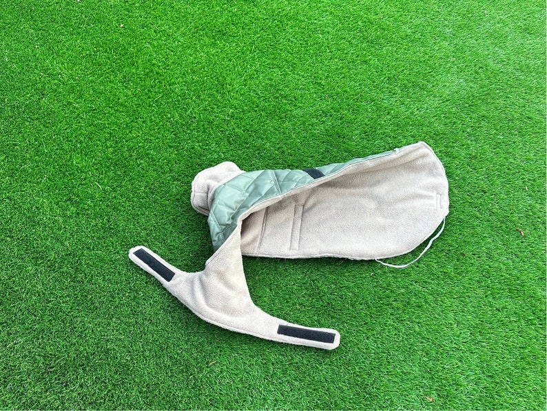 May include: A green and beige quilted dog coat with a fleece lining. The coat has a zipper closure and adjustable straps.