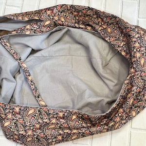 Op de afbeelding: Een grijs hondenbed van stof met een paisley-rand in tinten zwart, rood en cr&egrave;me.
