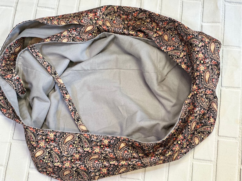Op de afbeelding: Een grijs hondenbed van stof met een paisley-rand in tinten zwart, rood en cr&egrave;me.