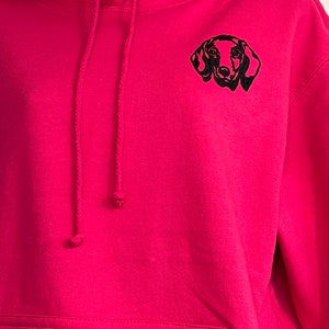 Op de afbeelding: Een roze hoodie met een zwarte geborduurde teckel op de voorkant.