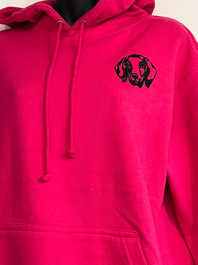Op de afbeelding: Een roze hoodie met een zwarte geborduurde teckel op de voorkant.
