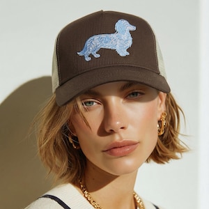 Può includere: Cappellino da camionista marrone con retro in rete beige chiaro e un cane bassotto ricamato in azzurro. Il cappellino ha una visiera curva e una chiusura a scatto.