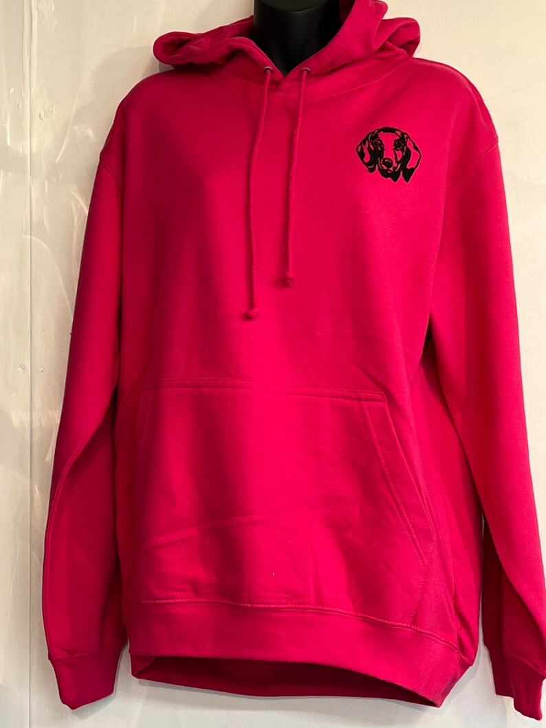 Op de afbeelding: Een roze hoodie met een geborduurd zwart silhouet van een teckel op de voorkant.