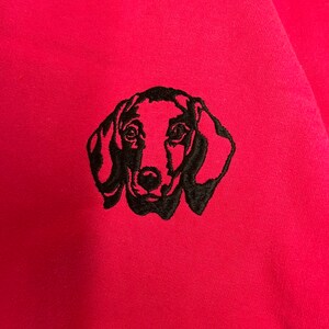 Op de afbeelding: Een zwart geborduurd dackel silhouet op een roze sweatshirt.