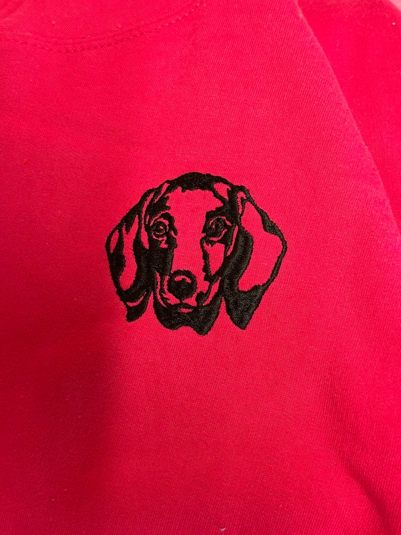 Op de afbeelding: Een zwart geborduurd dackel silhouet op een roze sweatshirt.