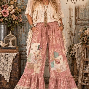 May include: Wide-leg trousers in a dusty rose colour with a bleached, mottled texture. The trousers feature various fabric patches, including floral and butterfly prints, and are finished with a wide, cream-coloured crocheted lace trim at the hem.