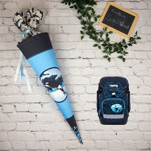Könnte beinhalten: Ein blauer und schwarzer Schulranzen mit einem weißen Logo, auf dem "ergobag" steht. Der Ranzen hat ein blaues und schwarzes Muster mit einem weißen Walmotiv. Ein blauer und weißer Schultüte mit einem weißen Walmotiv und dem Text "Endlich Schulkind" auf einer schwarzen Tafel.