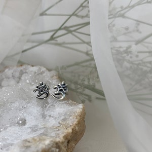 May include: A pair of silver Om symbol stud earrings on a white crystal rock.