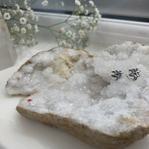 May include: A pair of silver Om symbol earrings displayed on a white crystal geode.