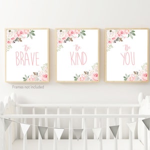 May include: Three framed prints with pink floral designs and white backgrounds. Each print features the text "Be" followed by a different word: "Brave", "Kind", and "You".