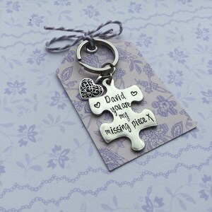 May include: Silver keychain with a heart charm and a puzzle piece charm. The puzzle piece charm has the text "David you are my missing piece x" engraved on it.