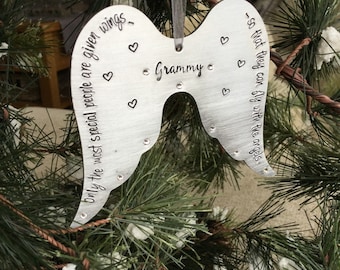 May include: A silver-colored angel wing ornament with the word "Grammy" and the phrase "Only the most special people are given wings - so that they can fly with the angels." The ornament has small heart and crystal accents.