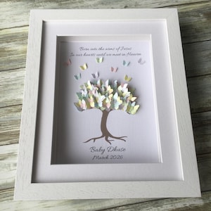May include: A framed artwork featuring a paper tree with butterfly-shaped leaves in pastel colors. The artwork includes the text "Born into the arms of Jesus, In our hearts until we meet in Heaven" and "Baby Dhuse, March 2026."