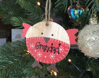 May include: A wooden Christmas ornament shaped like a bird with a red body and white snowflakes. The ornament has the word "Granddad" written on it in black.