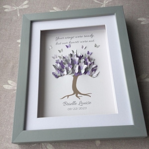 May include: A framed artwork featuring a tree with a butterfly-filled canopy in shades of purple, silver, and white. The tree trunk is brown, and the frame is gray. Text reads, "Your wings were ready, but our hearts were not." Below the tree is the name "Brielle Louise" and the date "09/22/2023."