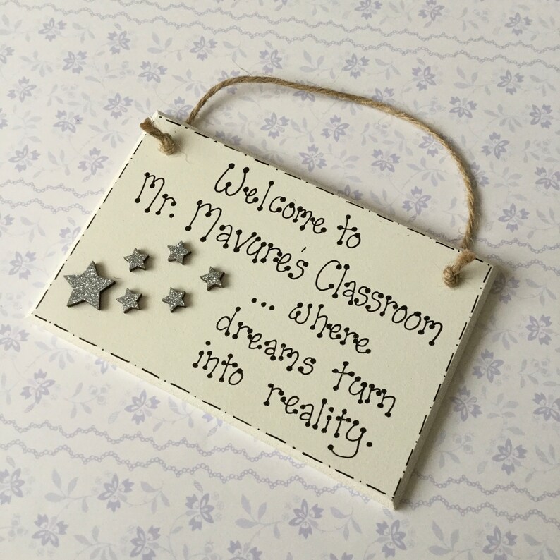 May include: Welcome to Mr. Mavure's Classroom... where dreams turn into reality. A white wooden sign with black lettering and silver glitter stars.