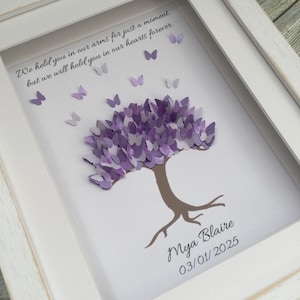 May include: A framed art piece featuring a tree with a purple butterfly-shaped canopy. The tree trunk and roots are brown. The artwork includes the text "We held you in our arms for just a moment, but we will hold you in our hearts forever." and the name "Mya Blaire" with the date "03/01/2025".