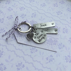 May include: Silver keychain with a heart charm, a round charm that says "This momma belongs to" and two rectangular charms with the names "Jonah" and "Violet" engraved on them.