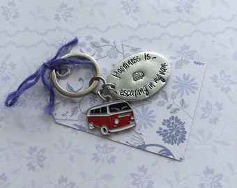 May include: Silver keychain with a red and white camper van charm. The keychain has a silver oval tag with the text "Happiness is escaping in my van".