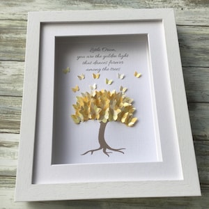 May include: A framed artwork featuring a paper tree with golden butterfly leaves and a brown trunk. The artwork includes the text "Little Orion, you are the golden light that dances forever among the trees." The frame is white.