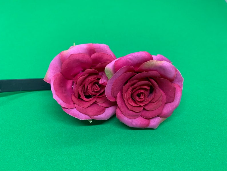 Peut inclure: Deux roses en tissu rose attach&eacute;es &agrave; un bandeau noir. Les roses sont superpos&eacute;es et ont un aspect r&eacute;aliste.
