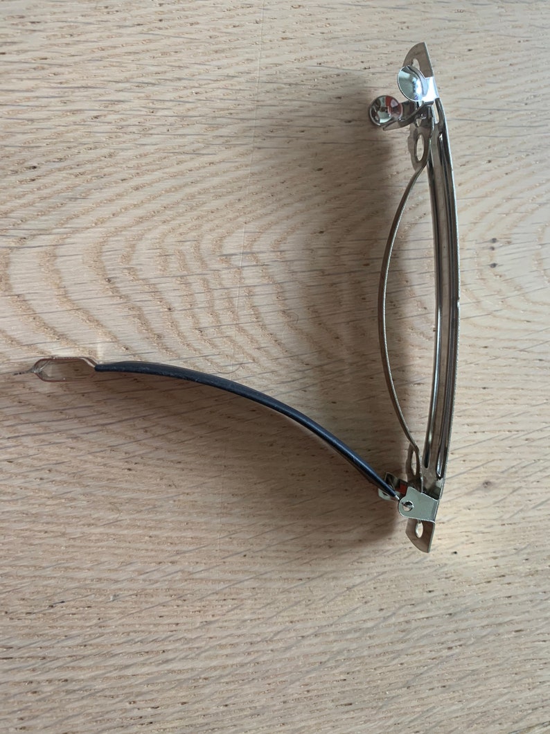 Peut inclure: Une pince &agrave; cheveux en m&eacute;tal argent&eacute; avec un &eacute;lastique noir. La pince est ouverte et pr&ecirc;te &agrave; &ecirc;tre utilis&eacute;e.