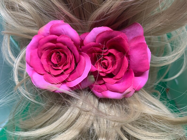 Peut inclure: Deux roses en tissu rose avec un centre rose l&eacute;g&egrave;rement plus fonc&eacute; sont attach&eacute;es &agrave; une queue de cheval blonde.