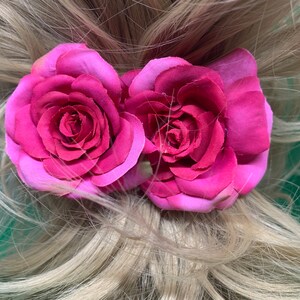 Peut inclure: Deux roses en tissu rose avec un centre rose l&eacute;g&egrave;rement plus fonc&eacute; sont attach&eacute;es &agrave; une queue de cheval blonde.