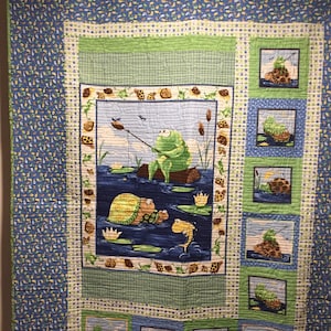 May include: A blue and green patchwork quilt with a central panel featuring a frog fishing and a turtle swimming. The surrounding panels feature smaller images of frogs and turtles.