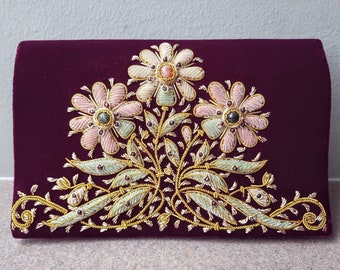 Könnte beinhalten: Eine Clutch aus violetter Samt mit goldener und silberner Stickerei von rosa Blumen. Die Blumen haben grüne und rosa Akzente und sind mit kleinen Edelsteinen verziert.
