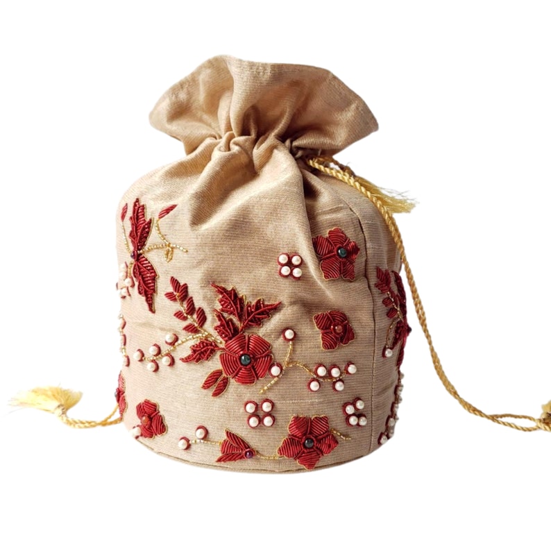 Op de afbeelding: Een beige trekkoordtas met gedetailleerde bloemenborduurwerk in rood en goud. De tas heeft een geplooid bovenstuk en een gouden trekkoord sluiting met kwastjes. Kleine witte kralen zijn verwerkt in het bloemendesign.