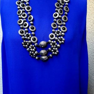 May include: A silver and black multi-strand necklace with round and oval beads. The necklace is layered and features a decorative design.