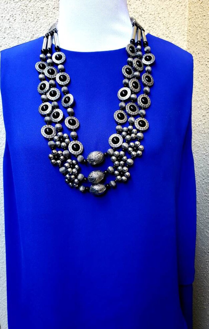 May include: A silver and black multi-strand necklace with round and oval beads. The necklace is layered and features a decorative design.