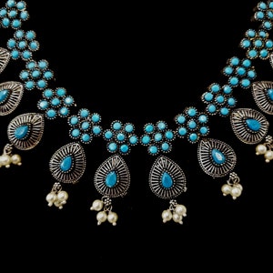 May include: A silver necklace with blue and white stones. The necklace has a teardrop design with multiple strands of pearls.
