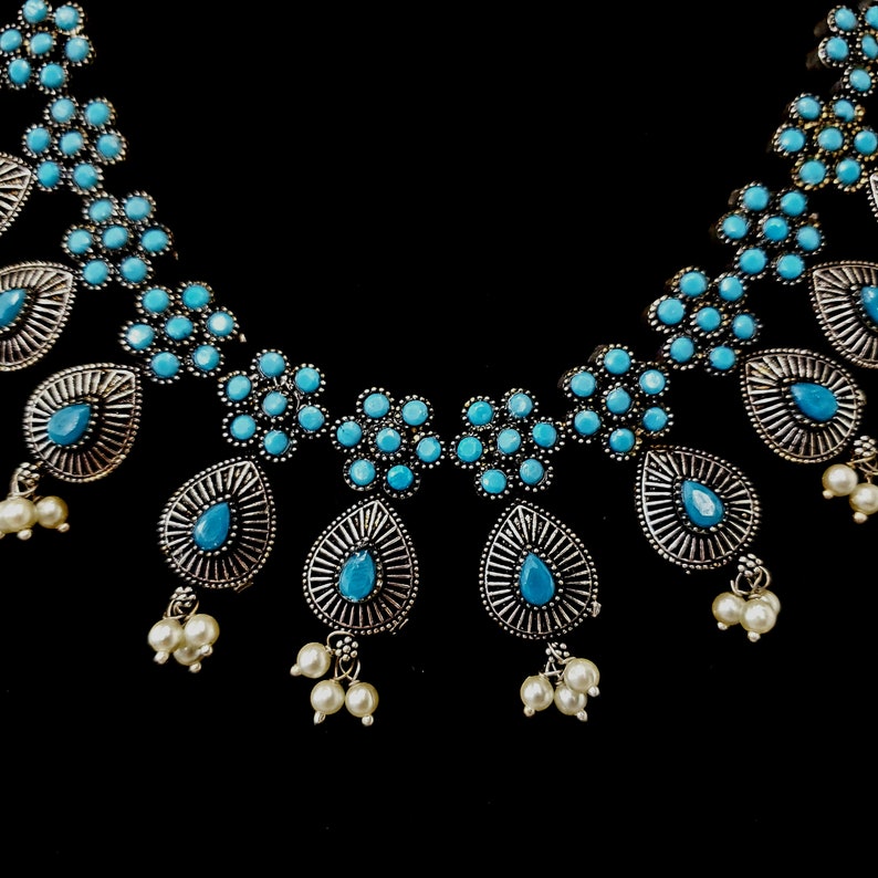 May include: A silver necklace with blue and white stones. The necklace has a teardrop design with multiple strands of pearls.
