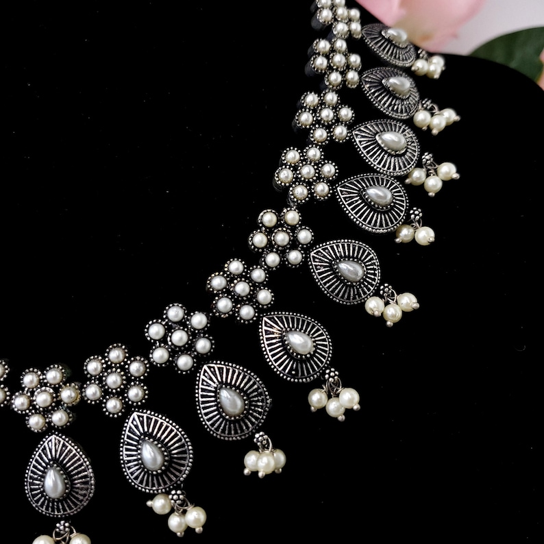 May include: A silver necklace with a teardrop design and white pearl accents. The necklace is made of metal and has a delicate, feminine look.
