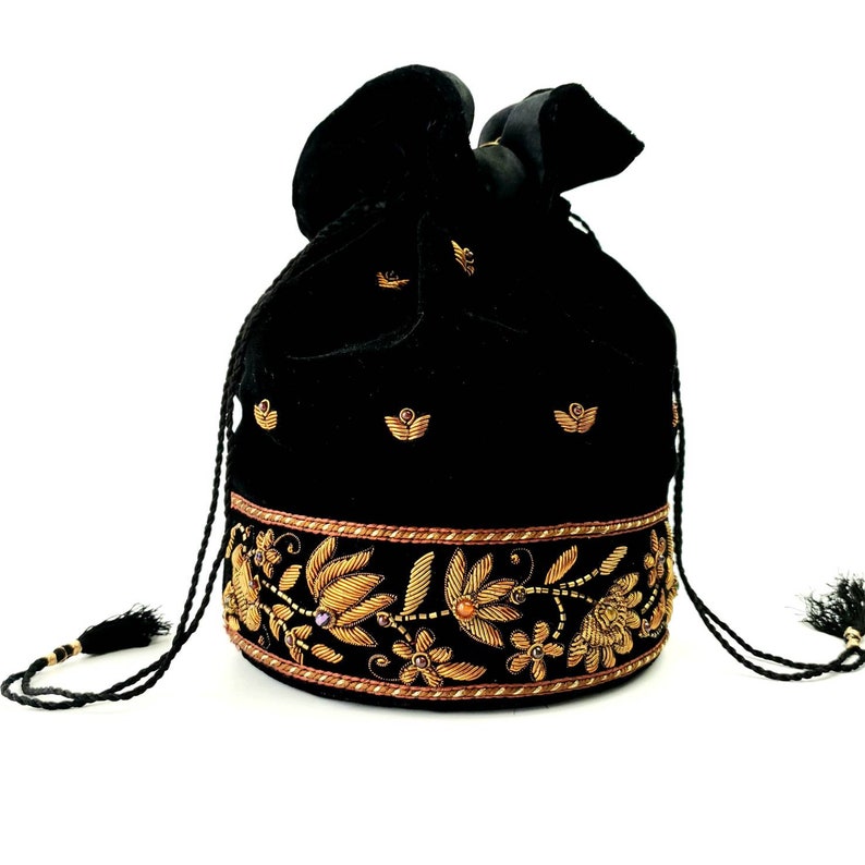 May include: A black velvet drawstring bag with gold embroidery featuring floral designs. The bag has a tassel on each side.
