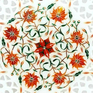 Puede incluir: Una mesa de m&aacute;rmol blanco con un dise&ntilde;o floral incrustado con piedras naranjas, verdes y rojas. El dise&ntilde;o presenta una estrella central rodeada de flores y hojas estilizadas.