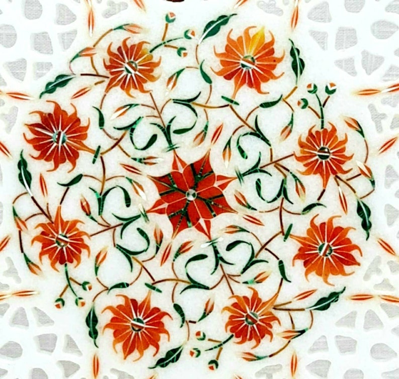 Puede incluir: Una mesa de m&aacute;rmol blanco con un dise&ntilde;o floral incrustado con piedras naranjas, verdes y rojas. El dise&ntilde;o presenta una estrella central rodeada de flores y hojas estilizadas.