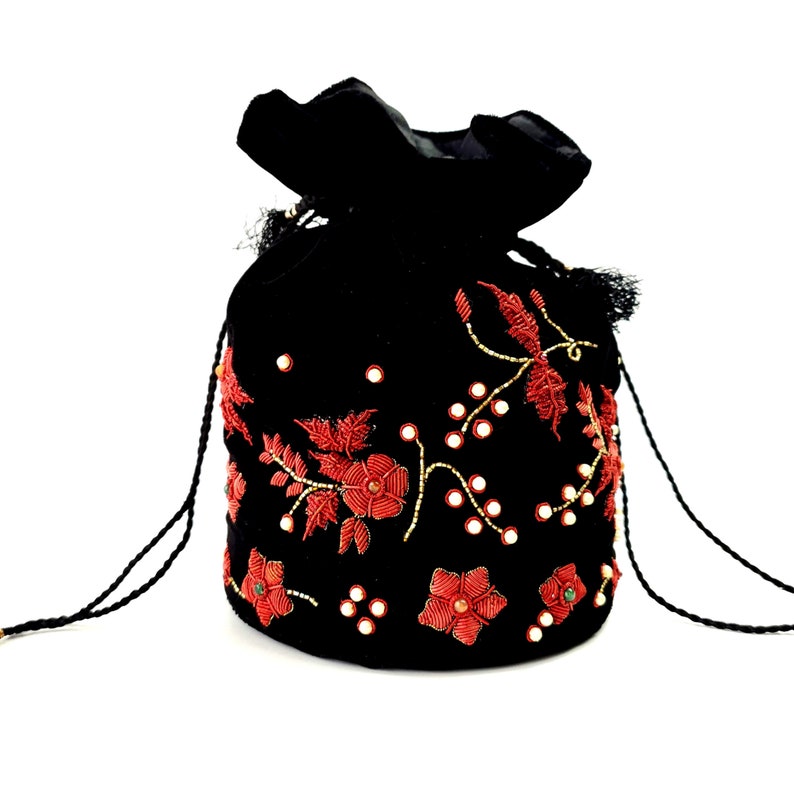 Op de afbeelding: Zwarte fluwelen trekkoordtas met rode bloemenborduursels en kralen. De tas heeft een geplooid bovenstuk en een getextureerde afwerking. Het ontwerp bevat kleine spiegels en goudkleurige kralen.