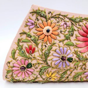 May include: A pink fabric clutch bag with embroidered floral designs in shades of pink, orange, yellow, green, and purple. The flowers have jeweled centers.