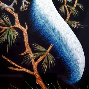 Puede incluir: Obra de arte bordada de un p&aacute;jaro azul y blanco posado en una rama con agujas de pino verdes y doradas. Las plumas de la cola del p&aacute;jaro son largas y fluidas.