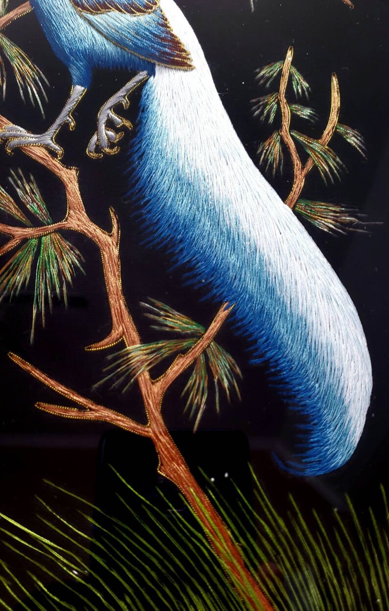 Puede incluir: Obra de arte bordada de un p&aacute;jaro azul y blanco posado en una rama con agujas de pino verdes y doradas. Las plumas de la cola del p&aacute;jaro son largas y fluidas.
