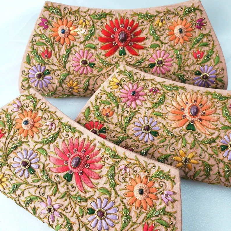 May include: Three beige fabric clutches with floral embroidery. The clutches feature a variety of colorful flowers with jeweled centers. The flowers are embroidered in shades of pink, orange, red, purple, and yellow.