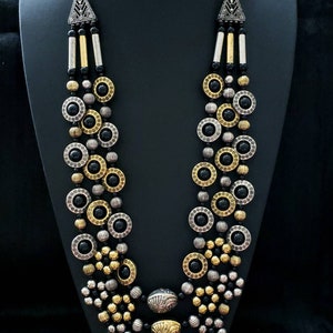 May include: A multi-strand necklace with black, gold, and silver beads. The necklace features round, patterned beads and a large, ornate pendant.