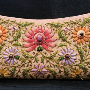May include: A light pink clutch purse with floral embroidery. The flowers are in shades of pink, orange, purple, and green. The purse is decorated with gold thread and small, colorful beads.