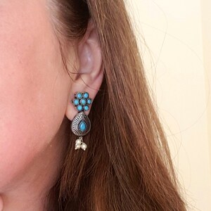 May include: A pair of silver earrings with turquoise stones. The earrings have a teardrop shape with a cluster of smaller turquoise stones at the top.