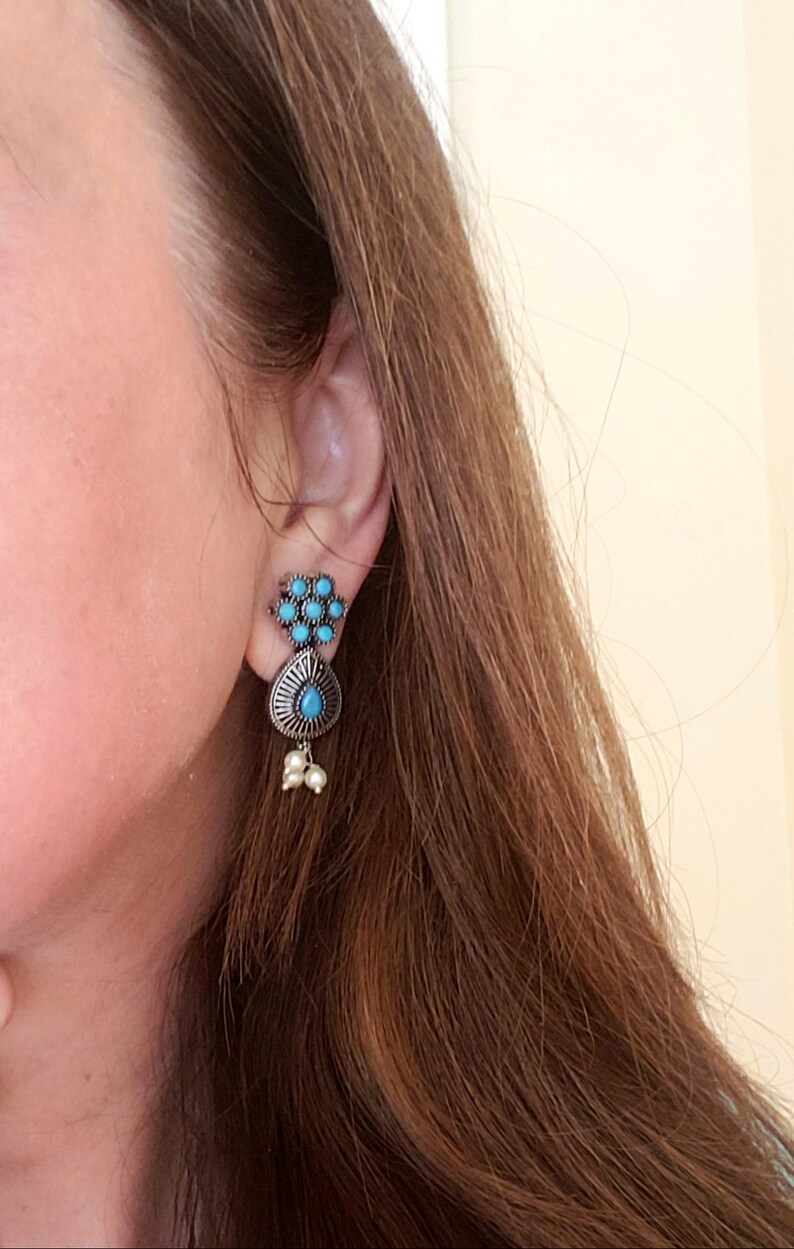 May include: A pair of silver earrings with turquoise stones. The earrings have a teardrop shape with a cluster of smaller turquoise stones at the top.