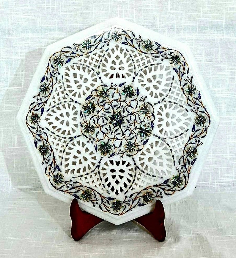 Puede incluir: Bandeja octogonal de m&aacute;rmol blanco con un intrincado dise&ntilde;o de corte y patrones florales incrustados en tonos de azul, verde y dorado. La bandeja est&aacute; sobre un soporte de madera.