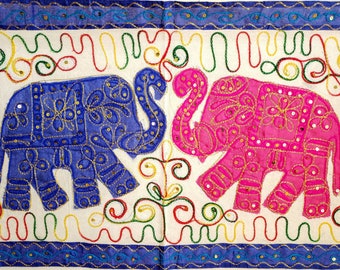 May include: Embroidered wall hanging featuring two elephants, one blue and one pink, with intricate floral designs and sequins. The elephants are facing each other on a white background with a colorful border.
